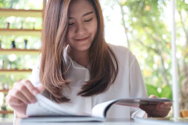 Güzel bir Asyalı kadın ile yeşil doğa arka plan beyaz modern kafede bir kitap okuma