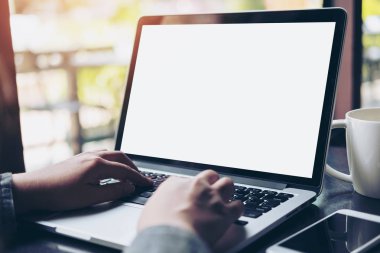 Mockup görüntüsünü kullanarak ve boş beyaz ekran ve modern loft kafede cam masada kahve fincanı ile laptop yazarak iş kadını