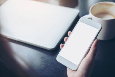 Hareket eden telefon ile latop ve kahve Kupası tahta masada boş beyaz ekran ile kafede tutan iş kadın görüntüsünü mockup