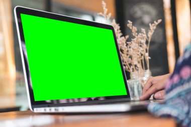 Ofiste ahşap tabloda boş yeşil ekranlı dizüstü bilgisayar kullanan bir kadın görüntüsünü mockup