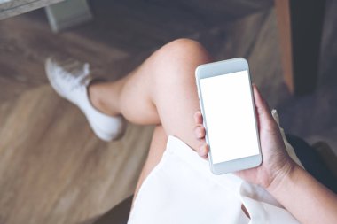 Modern ahşap zemin arka plan ile uylukta boş ekran ile beyaz cep telefonu tutan kadının el mockup görüntü