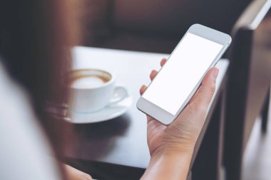 Boş beyaz ekran ve sıcak kahve Kupası ahşap masa üzerinde cep telefonu kafede holding eller mockup görüntü