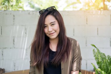 Portre portre resim beyaz tuğla duvar arka plan ile park açık oturuyor ve gülümseyen güzel bir Asyalı kadın