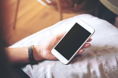 Yastık ile ahşap zemin arka plan üzerinde beyaz cep telefonu ile boş siyah perde holding eller mockup görüntü