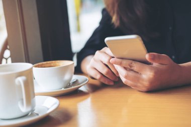 Bir kadınla tutarak ve ahşap masa kafede kahve Kupası ile akıllı telefon kullanarak gülen yüz