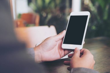 Ahşap masa üzerinde sıcak kahve fincanı ile boş beyaz ekran ile beyaz cep telefonu kafede holding eller mockup görüntü