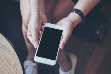 Modern ahşap zemin arka plan ile uylukta boş siyah perde ile beyaz cep telefonu tutan kadının el mockup görüntü