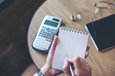 Bir kadın tutarak ve ahşap ofiste tabloda tablet ile boş defter üzerinde yazma görüntüsünü üstten görünüm
