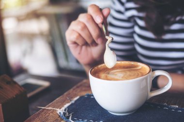 Sıcak kahve üzerinde ahşap masa karıştırın kahve kaşık tutan bir kadın