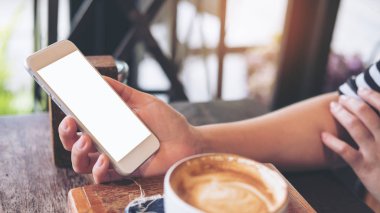 Kafede kahve fincanı ahşap tablo ile boş ekran ile beyaz cep telefonu tutan el mockup görüntü