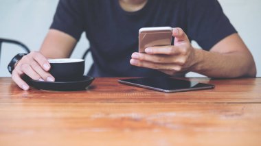 Akıllı telefon ve holding kahve Kupası modern Café kullanan bir adam