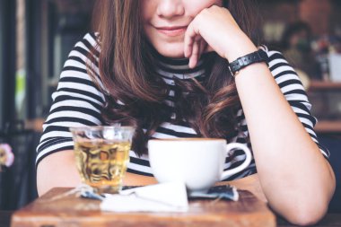 Bardak sıcak kahve ve çay vintage ahşap masa ile kafede oturan bir Asyalı 