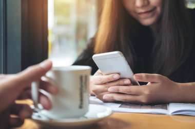 Kullanarak ve bir fincan kahve ön planda tutan bir el ile akıllı telefon kafede bakarak gülen yüz ile güzel bir Asyalı kadın