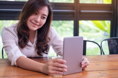 Güzel Asyalı kadın ile gülen yüz tutan ve yeşil doğa arka plan ile modern kafede tablet PC'yi kullanma