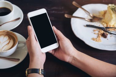 Beyaz cep telefonu ile boş siyah perde ile kahve fincanı ahşap tablo lokantada holding eller mockup görüntü