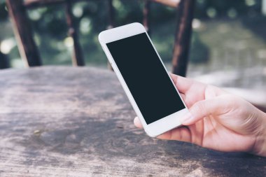 Sıcak kahve Kupası ahşap masa üzerine boş siyah perde ile beyaz cep telefonu kafede holding eller mockup görüntü