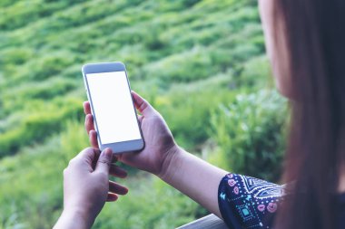 Bir kadın tutarak ve açık ve yeşil doğa arka plan boş ekran ile beyaz akıllı telefon kullanarak mockup görüntü