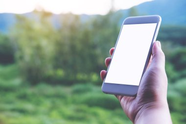 Mockup görüntü tutarak ve açık ve yeşil doğa arka plan beyaz akıllı telefon boş ekran ile gösterilen bir el