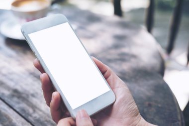 Antika ahşap masa ve doğa arka plan üzerinde beyaz cep telefonu ile boş perde holding eller mockup görüntü