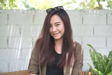 Portre portre resim beyaz tuğla duvar arka plan ile park açık oturuyor ve gülümseyen güzel bir Asya kadının