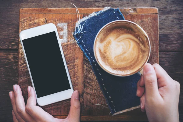 Kafede cep telefonu ile boş siyah perde ve kahve fincanı vintage ahşap masa üzerinde tutan bir el mockup görüntü