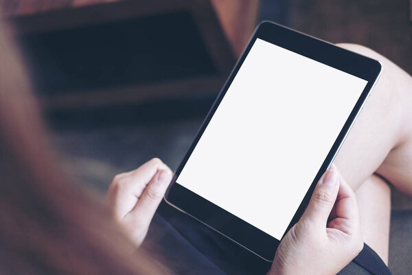 Mockup image of woman's hand holding black tablet pc with blank white screen on thigh in modern cafe