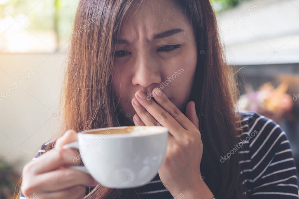 Closeup image of Asian woman holding hot coffee with feeling strange and smelling bad in coffee shop