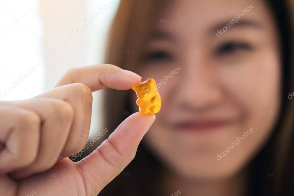 Closeup image of a beautiful Asian woman smiling , holding and looking at orange gummy bear 