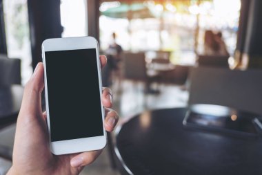 Mockup görüntü tutarak ve beyaz cep telefonu kafede boş siyah perde ile yükselterek el