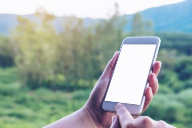 Mockup görüntü tutarak, tuşuna basarak ve açık ve yeşil doğa arka plan boş ekran ile beyaz akıllı telefon kullanarak bir el