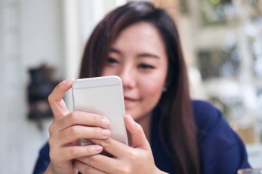 Güzel Asyalı kadın ile kullanarak ve modern café'akıllı telefon bakarak gülen yüz