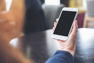 Kafede masada boş siyah perde ile beyaz cep telefonu tutan el mockup görüntü