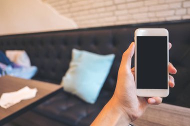 Mockup görüntü tutarak ve beyaz cep telefonu ile modern kafede boş siyah perde yükselterek bir el