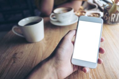 Kafede beyaz cep telefonu ile boş perde ve kahve fincanı insanlarla ahşap masa üzerinde tutan el mockup görüntü