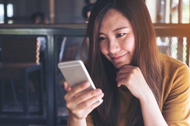 Kullanarak ve modern café'akıllı telefon bakarak gülen yüz ile güzel bir Asyalı kadın