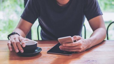 Akıllı telefon ve holding kahve Kupası modern Cafe ahşap tablo kullanan bir adam
