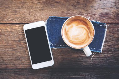 Mockup görüntü ile boş siyah perde ve sıcak latte kahve Cafe antika ahşap masa üzerinde beyaz cep telefonu