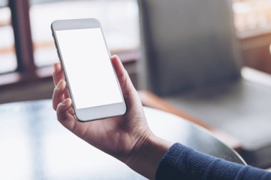 Kafede masada boş bir ekran ile beyaz cep telefonu tutan el mockup görüntü