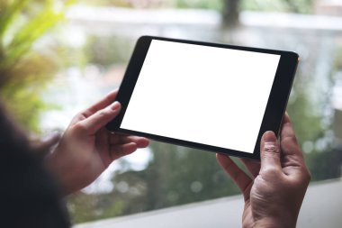 Yeşil Doğa arka plan ile modern kafede siyah tablet pc ile beyaz boş perde holding eller mockup görüntü