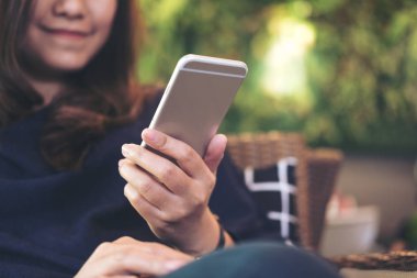 Kullanarak ve yeşil dikey bahçe arka plan ile modern café'akıllı telefon bakarak gülen yüz ile güzel bir Asyalı kadın