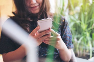 Kullanarak ve yeşil doğa arka plan ile modern café'akıllı telefon bakarak güzel bir Asyalı kadın