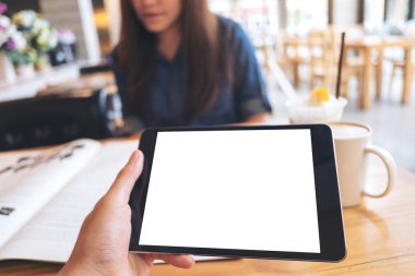 Görüntü kadın modern café arka planda gazete okuma ile siyah tablet pc ile beyaz boş ekran ve kahve fincanı ahşap masa üzerinde tutan bir el kadar alay 