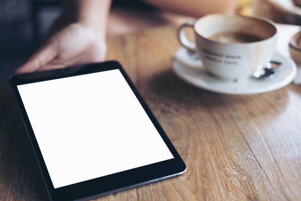 Образец изображения рук, держащих, показывающих и дающих черный планшет ПК с чистым белым экраном somwone на винтажном деревянном столе с чашкой кофе
