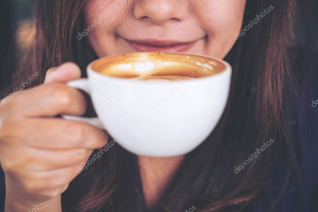 Closeup image of Asian woman smelling and drinking hot coffee with feeling good in cafe