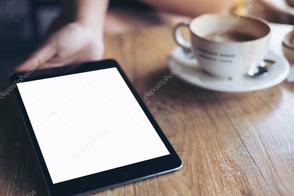 Mockup image of hands holding , showing and giving black tablet pc with blank white screen to somwone on vintage wooden table with coffee cup