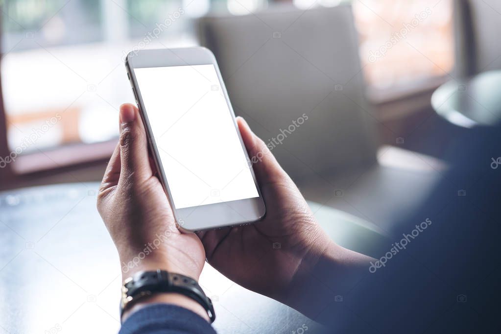 Mockup image of hands holding mobile phone with blank white screen in vintage cafe