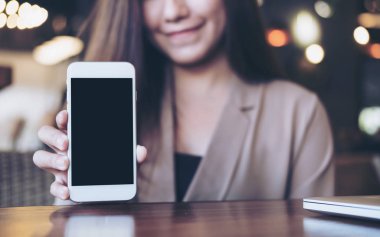 Holding ve boş siyah perde ve gülen yüz ile beyaz cep telefonu kafede gösterilen bir güzel Asya iş kadını mockup görüntü