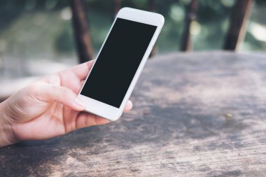 Sıcak kahve Kupası ahşap masa üzerine boş siyah perde ile beyaz cep telefonu kafede holding eller mockup görüntü