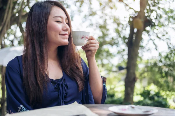 A beautiful Asian woman close her eyes smelling and drinking hot coffee with feeling good with green nature background