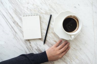 Bir elin en üstteki görüntüsü boş beyaz bir deftere kahve fincanı ile yazılacak.